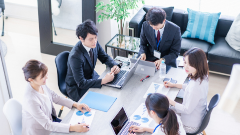 明るい雰囲気の部屋で5人のビジネスパーソンが会議を行っています。